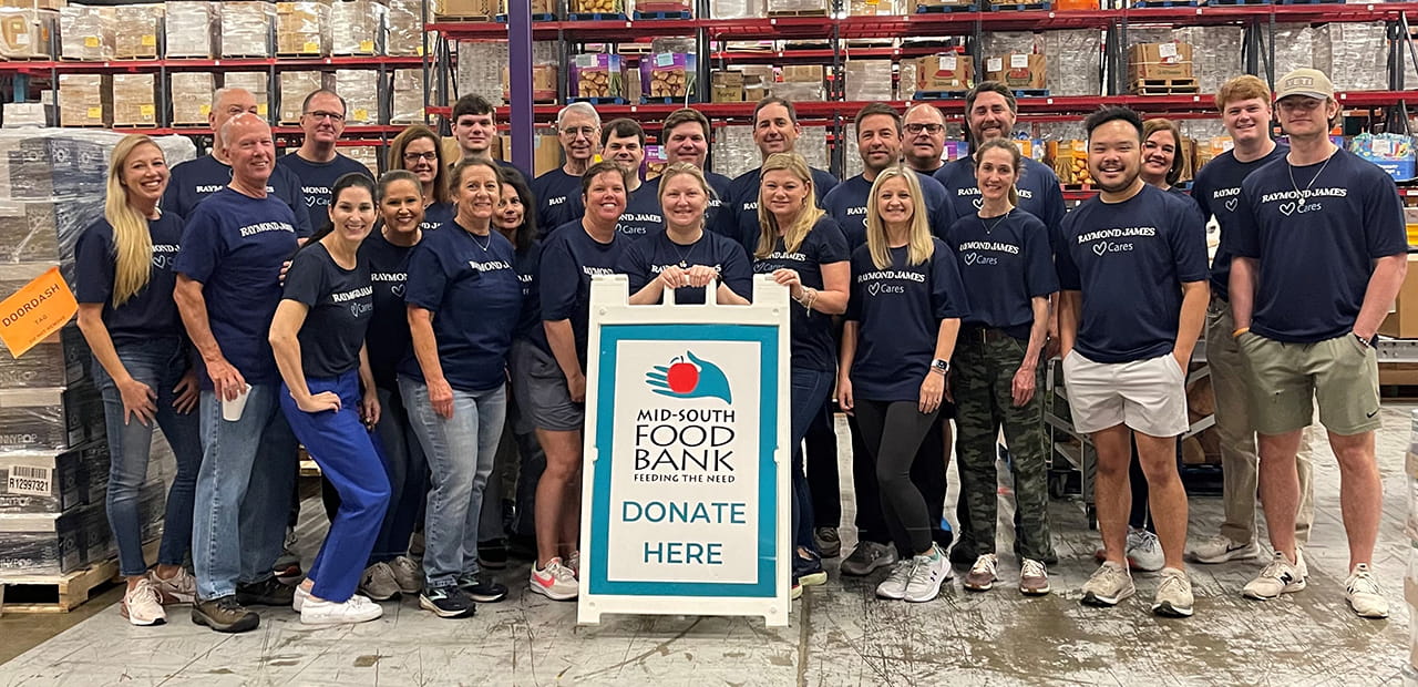 A group of smiling Raymond James associates stands together wearing Raymond James Cares shirts